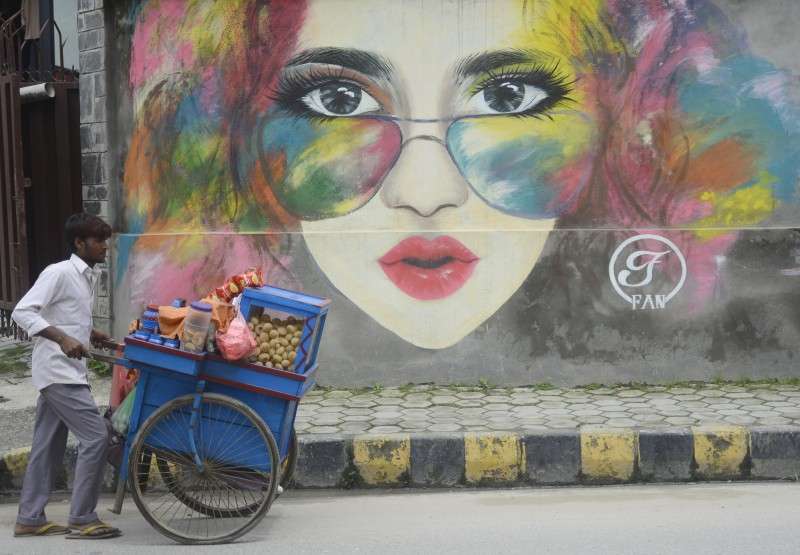 A street vendor moving a portable ‘chatpate’ snacks stall against the backdrop of a wall paint in Kupondole. Photo: Ravi Maharjan/NBA